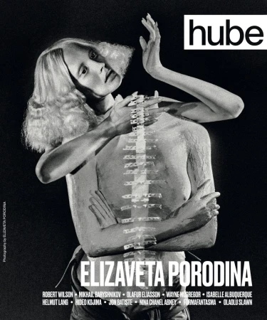 Monochrome portrait of a light-skinned woman with blonde hair and body paint, appearing as a magazine cover against a dark background.