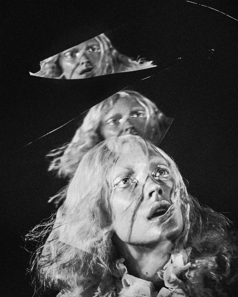 Monochrome portrait of a young adult woman with fair skin and long blonde hair looking upward, with mirrored reflections above.