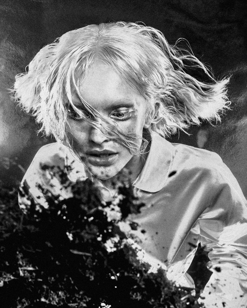 High-angle shot of a woman with wavy blonde hair and a collared shirt, looking down at dark, textured material covering the lower frame.