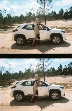 White SUV parked on sandy terrain with a woman opening the driver's side door, backed by a forest under a blue sky.