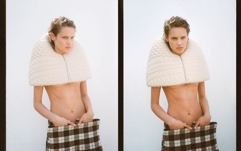 A person with short hair wears a knit collar and a plaid skirt, striking a confident pose against a bright white backdrop in a studio shot.
