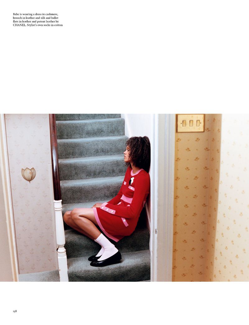 Woman in a red dress, white socks, and black shoes sits on gray stairs in an indoor setting with patterned wallpaper.