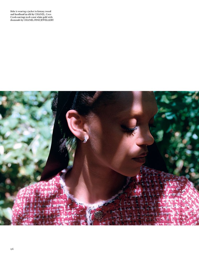 Close-up of a young Black woman wearing a tweed jacket and diamond earrings, with dark hair and soft lighting in a natural setting.