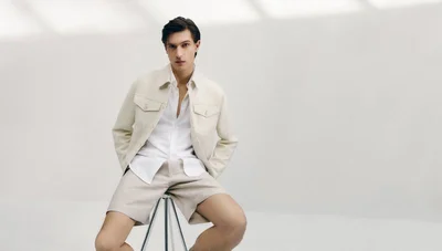 Male model seated on a stool wearing a white shirt and cream jacket against a white backdrop for BOSS.