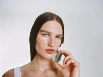 Woman holding a dropper bottle of Goop Hydration Serum against a white background