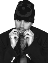 Monochrome portrait of Romeo Beckham wearing a graphic black beanie and dark blazer against a clean white backdrop.