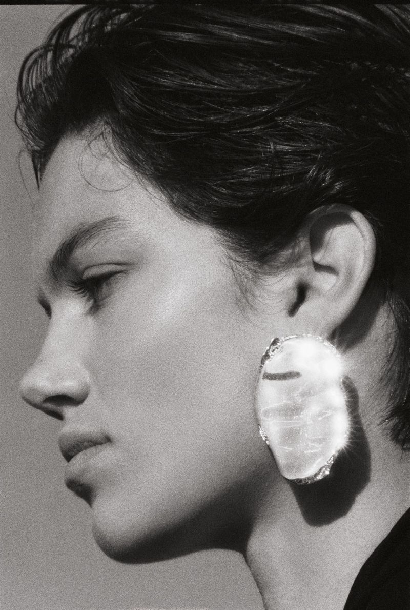 Monochrome portrait of a woman in profile wearing a statement earring against a plain background in a beauty and fashion context.
