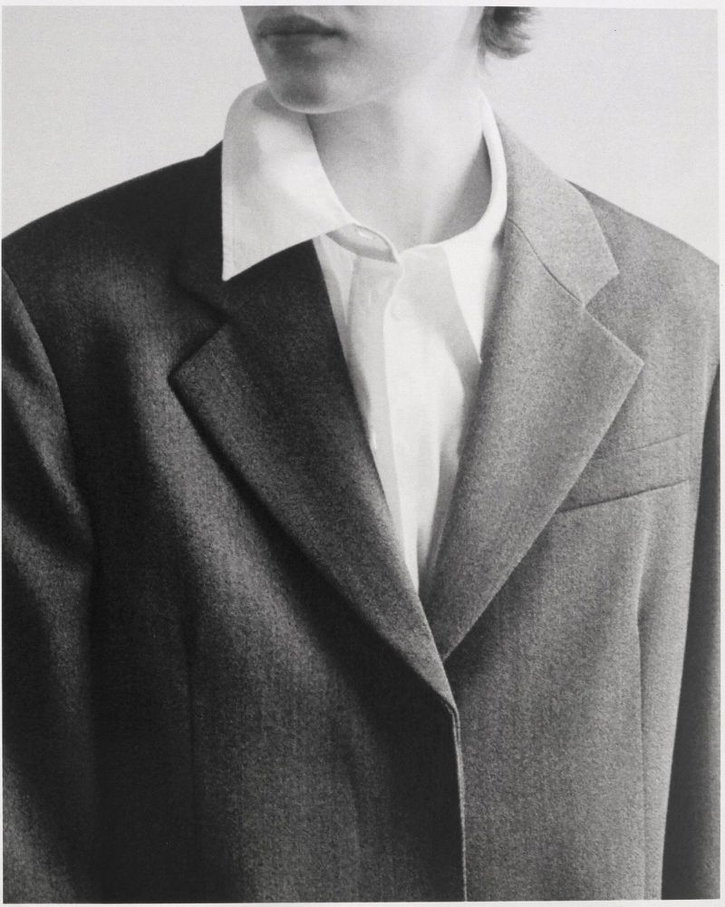 Close-up fashion shot of a person wearing a white shirt and grey blazer, focusing on the garment's textures and monochrome color palette.