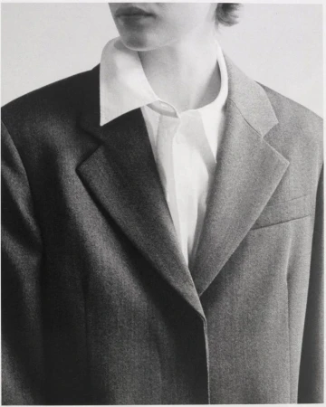 Close-up fashion shot of a person wearing a white shirt and grey blazer, focusing on the garment's textures and monochrome color palette.