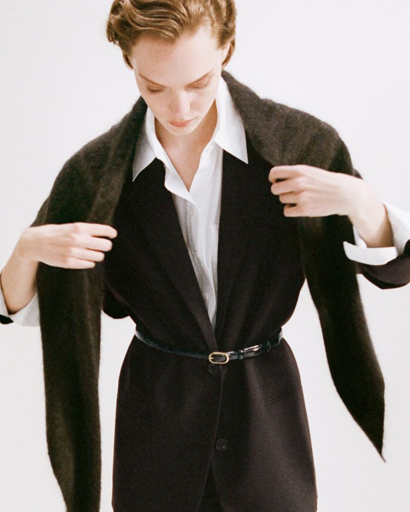 Fashionable woman in a black blazer with a white shirt and a brown scarf posing in a photo studio with soft lighting.