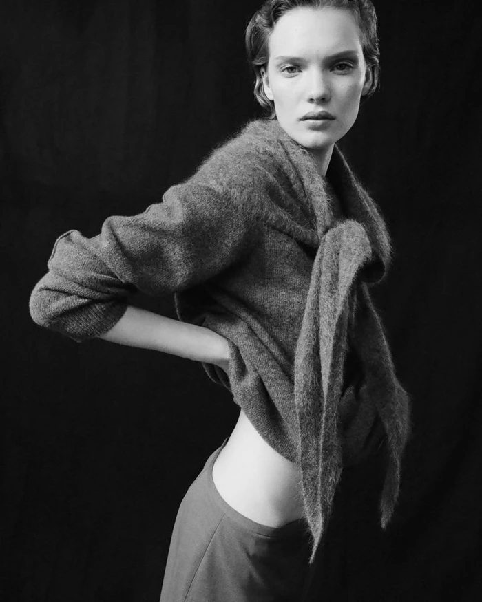 Model in textured grey sweater posing against dark background for COS editorial