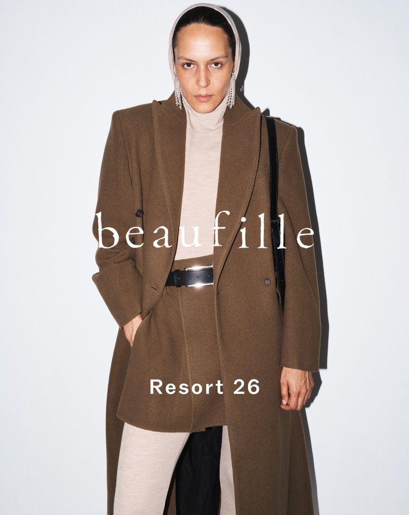 Model Laura Rylands wearing a tailored brown coat, mini skirt, and cream turtleneck against a white background for Beaufille Resort 26.