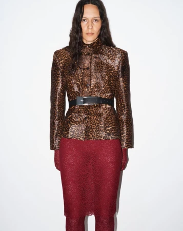 Fashion shot of a woman wearing a leopard print jacket, black belt, and red lace skirt, posing against a white background.