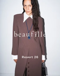 Model Laura Rylands wearing a brown structured long dress with a white collar and blue beaded necklace for beaufille Resort 26.