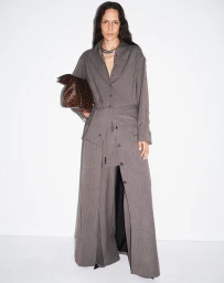 Model in grey matching long-sleeve shirt and wide trousers holding a brown textured handbag against a plain white background
