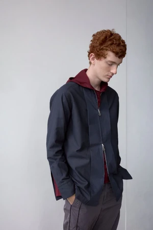 Jesse Sachet-Dufraisse wearing a navy zip overshirt with burgundy underlayer against a minimal light studio wall for Derrick S/S 26.