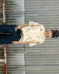 Model wearing a patterned t-shirt and dark jeans standing against corrugated metal siding for Pull and Bear STWD Denim