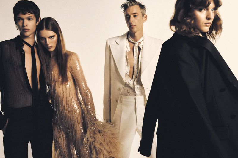 Four fashion models pose in a photo studio against a seamless backdrop, wearing stylish suits and dresses in a fashion editorial shoot.