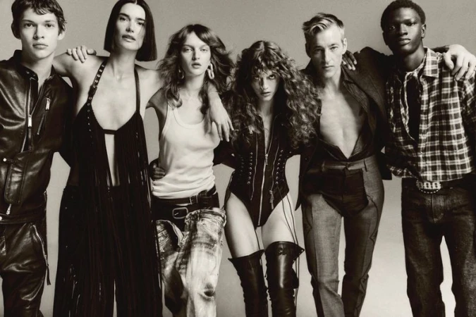 Editorial fashion shot of a diverse group of six young adults with their arms around each other, posing in a studio with a gray background.