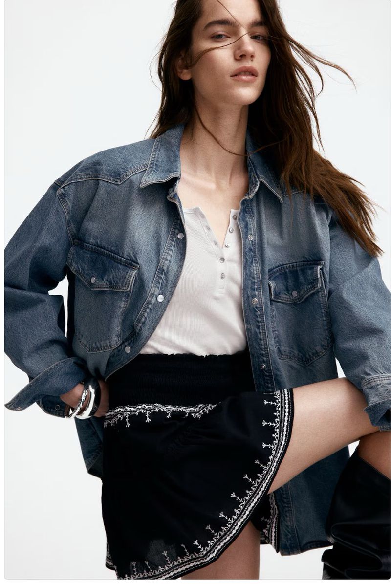 Fashion shot of a woman wearing a blue denim jacket, white top, and black miniskirt, posing in a studio setting. Beauty, fashion, style.
