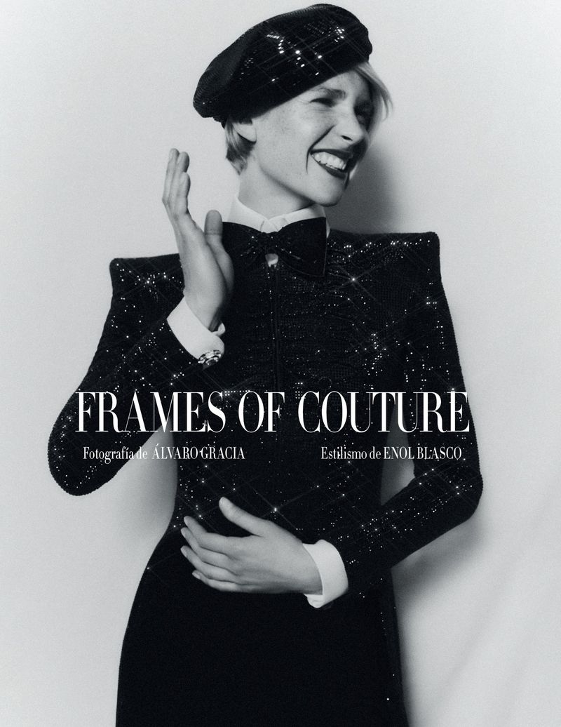Glamorous woman in a black sequined dress and beret smiles with hand raised in a fashion studio portrait against a light backdrop.