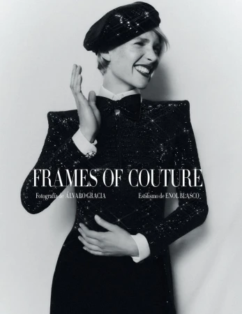 Glamorous woman in a black sequined dress and beret smiles with hand raised in a fashion studio portrait against a light backdrop.