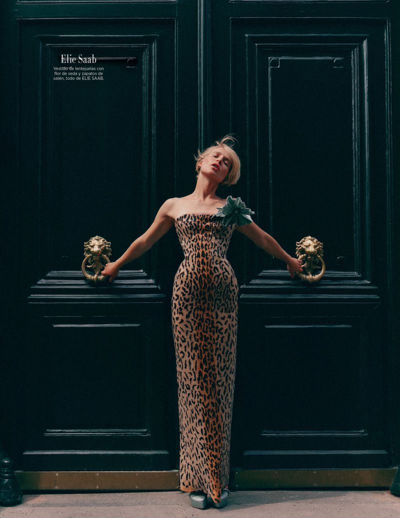 Elegant blonde woman in an animal-print gown poses in front of a large, dark door with lion-head knockers in a fashion editorial.