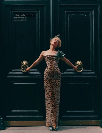 Elegant blonde woman in an animal-print gown poses in front of a large, dark door with lion-head knockers in a fashion editorial.