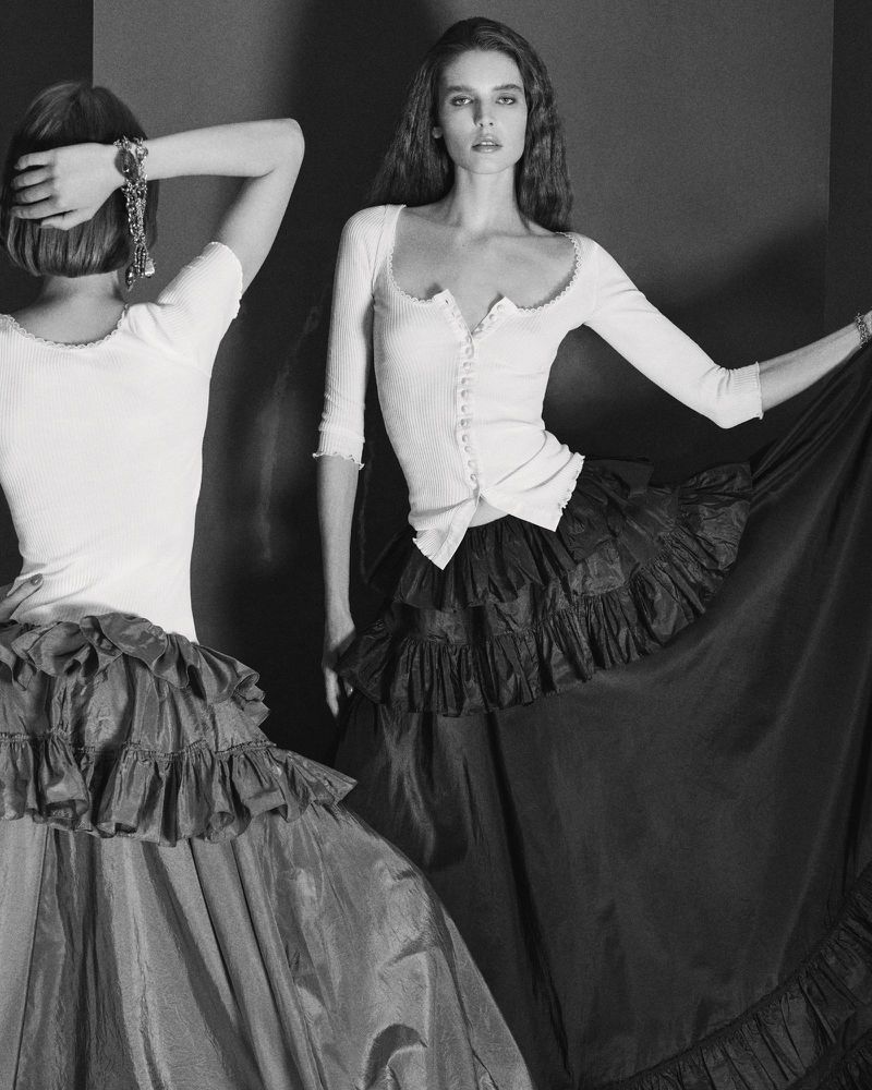 Two women in ruffled skirts and fitted tops pose in a black and white fashion shot, showcasing textures and elegant silhouettes.