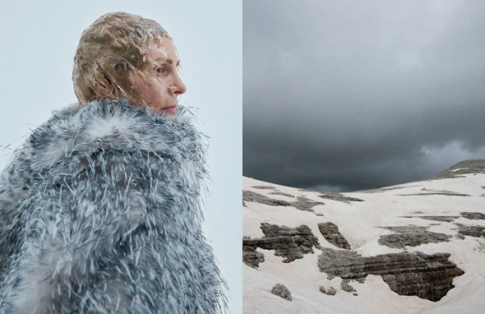 Profile view of a woman with elaborate hair and a grey feather coat, contrasted with a snow-covered mountain landscape under an overcast sky.
