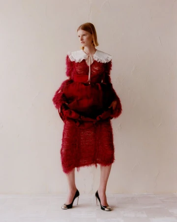 Woman in red textured dress and black heels poses against a neutral wall. The fashion shot features a white collar and unique details.