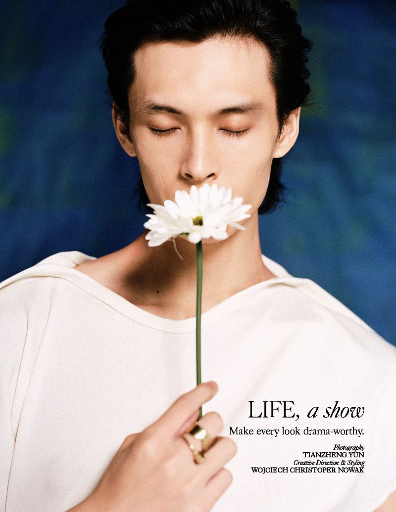 Asian man holding a white daisy near his face against a dark blue textured background for L'Officiel Malaysia.