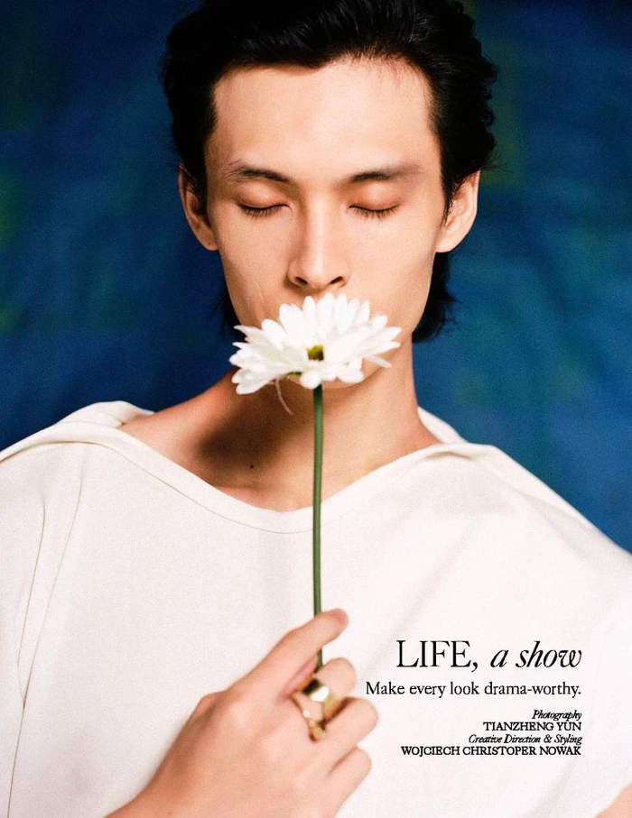Asian man holding a white daisy near his face against a dark blue textured background for L'Officiel Malaysia.