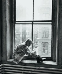 Monochrome image of model Fernanda Ly seated on a deep window sill with city buildings visible outside