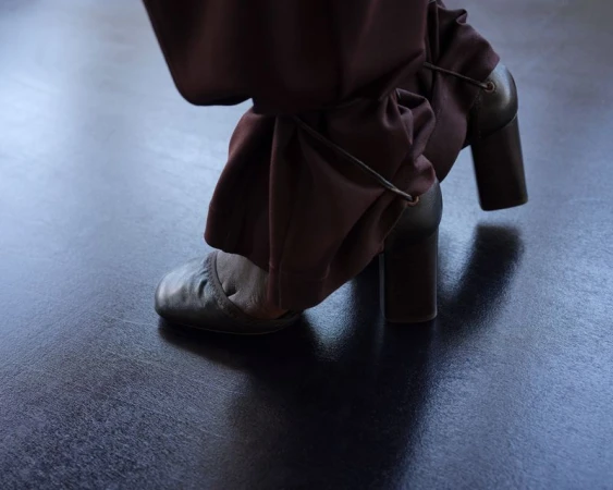 Close-up of brown heeled shoes and gathered trousers on a dark floor for Lemaire SS25 lookbook