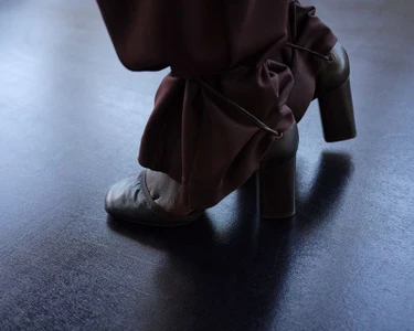 Close-up of brown heeled shoes and gathered trousers on a dark floor for Lemaire SS25 lookbook