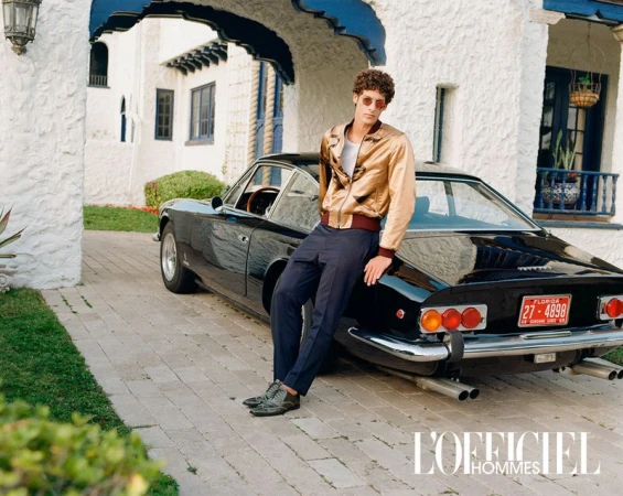 A male model poses with a black vintage car in front of an ornate white building, wearing a gold jacket and sunglasses, L'Officiel Hommes.