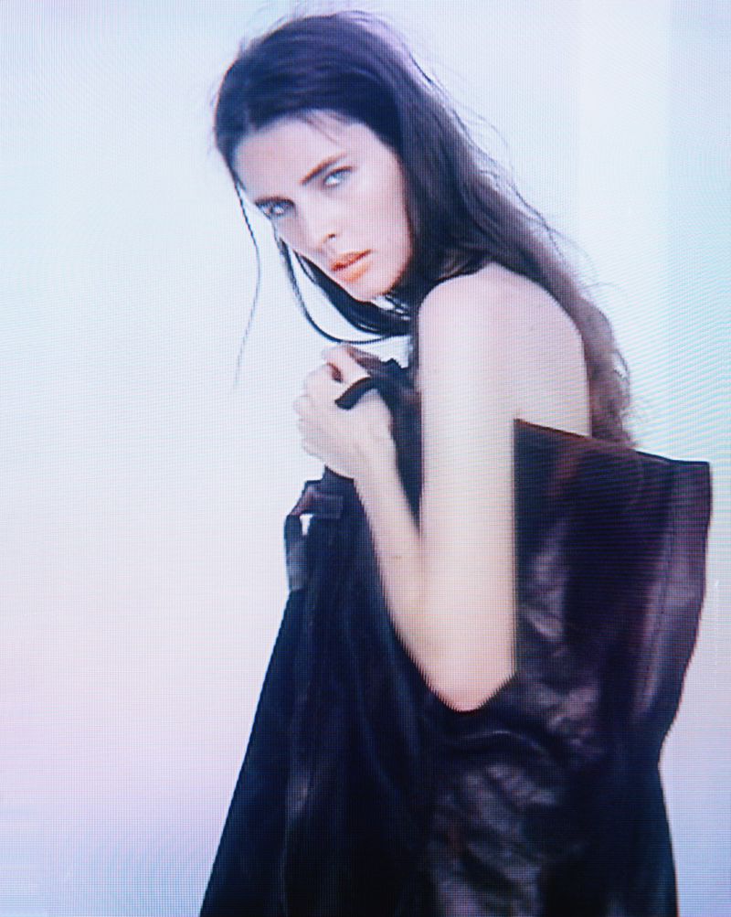 Portrait of a young adult female fashion model with long dark hair and wearing a dark top, gazing intently into the camera.