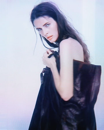 Portrait of a young adult female fashion model with long dark hair and wearing a dark top, gazing intently into the camera.