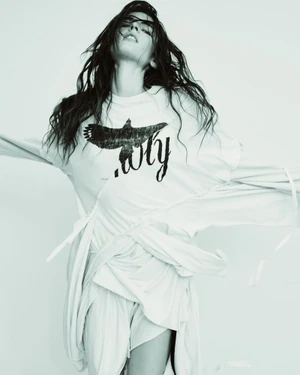 Model Libby Taverner posing dynamically in a draped white graphic t-shirt dress against a bright white background.