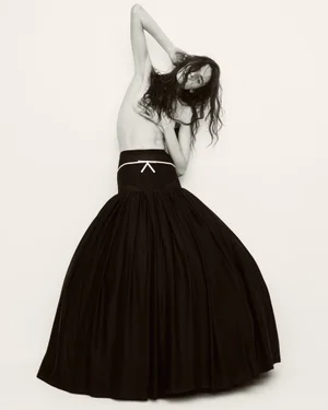 Model Libby Taverner wearing a full black skirt with white bow detail against a white background for Harper's Bazaar France.