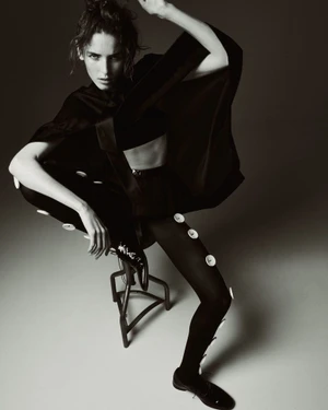 Model perched on a stool wearing a black outfit with white buttons for Harper's Bazaar France by Drew Vickers
