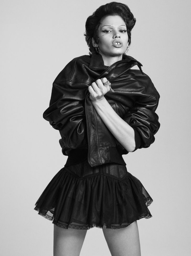 Model posing in an oversized black leather jacket and black pleated mini skirt in a monochrome fashion portrait.