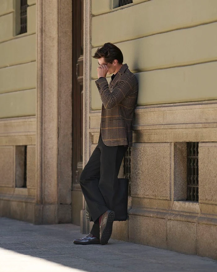 Model leaning against a stone building exterior wearing a patterned blazer and loafers for Tod's Accessories Campaign