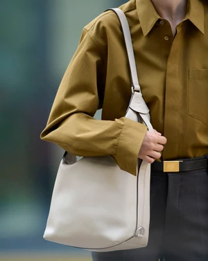Close-up of a person wearing an olive green shirt and carrying a cream leather shoulder bag for Tod’s accessories campaign.