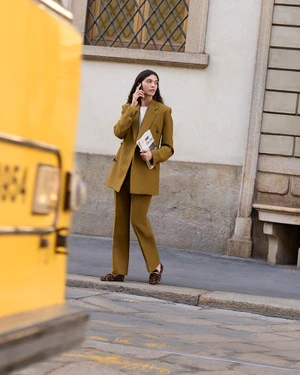 Model in olive green suit on a city street holding a newspaper and calling on a phone