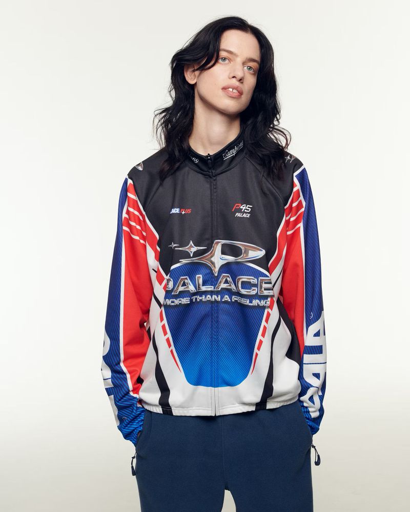 Person wearing a Palace brand racing-style jacket with red, white, and blue accents in a studio setting, medium shot on white background.