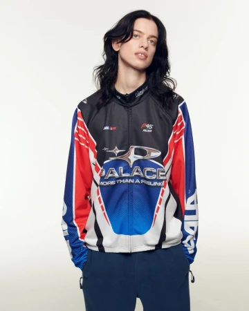 Person wearing a Palace brand racing-style jacket with red, white, and blue accents in a studio setting, medium shot on white background.