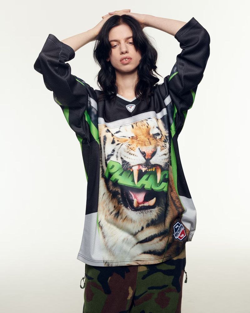 Young adult woman with her hands behind her head wearing a sports jersey with a tiger graphic on a white background.