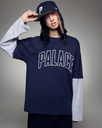 Model Lily McMenamy wearing a navy long-sleeve Palace t-shirt and baseball cap against a plain grey studio backdrop.